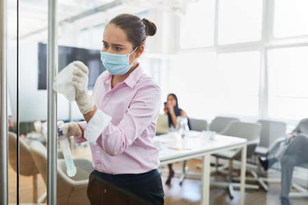 Cleaning lady with face mask because of Covid-19 when disinfecting in the office with disinfectantの写真素材