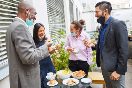 Group of business people eating snacks during lunch break with face mask on chin