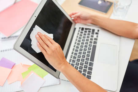 Hand of a businesswoman disinfecting at the PC monitor because of Covid-19 and corona virus in the...