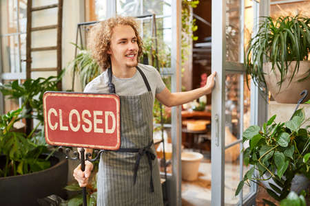 Young florist or gardener in front of garden center with the sign Closedの写真素材