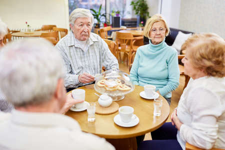 Group of seniors in the retirement home drinking coffee and talking in the common roomの写真素材