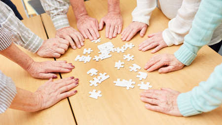 Hands of seniors on a table with puzzle pieces as memory trainingの写真素材