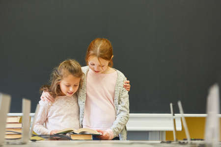 Two girls as elementary school students learn to read together in the classroom