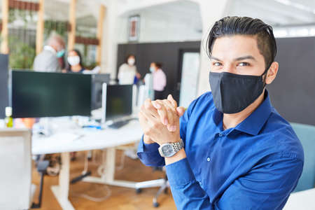 Young business man in the office with mouth and nose protection because of Covid-19 and coronavirus pandemicの写真素材
