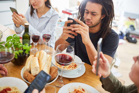 Friends look at social media websites on smartphone while eating at the tableの写真素材
