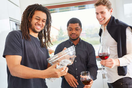 Young man drying dishes with tea towel in kitchen next to friends with red wineの写真素材