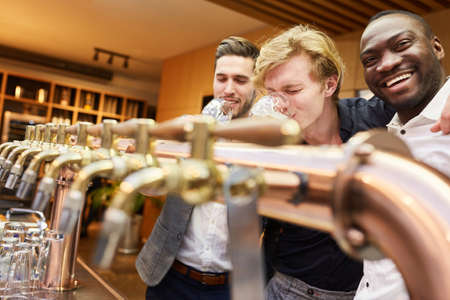 Three men at the counter in a pub drinking beer as men's evening