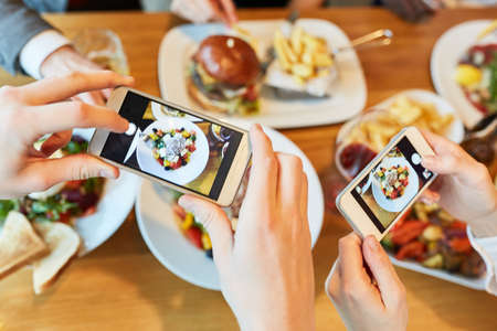 Hands with smartphones photograph food on table in restaurantの写真素材