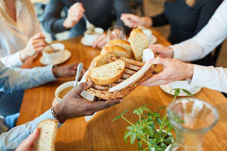 Hands distribute bread to soup while having lunch or dinner together