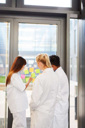 Medical team in front of glass with sticky notes with creative ideas in brainstorming seminar