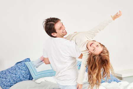 Father picks up his daughter and plays flies with her in the morning in the bedroomの写真素材