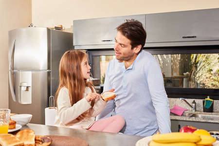 Father and his daughter in the morning in the kitchen with the bread smeared for breakfastの写真素材