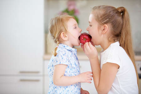 Two children eat a red apple together in the kitchenの写真素材
