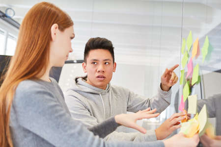 Young business people discuss ideas on sticky notes in brainstorming workshop