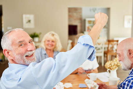 Cheering senior clenches his fist as a winner when playing cards in the retirement home