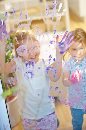 Children use finger paint to paint their hands on a glass pane in kindergartenの写真素材