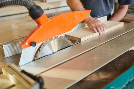 Craftsman pushes wood board on the circular saw in the carpentry or joinery