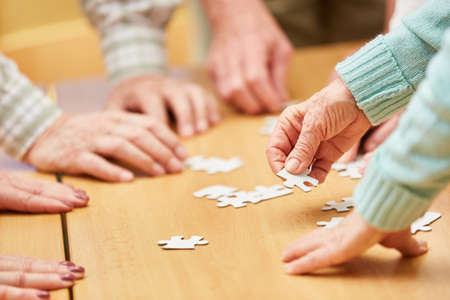 Hand of a senior citizen holds a piece of the puzzle while playing a puzzle in a retirement homeの写真素材