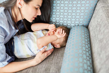 Mother lovingly takes care of tired child on living room sofa