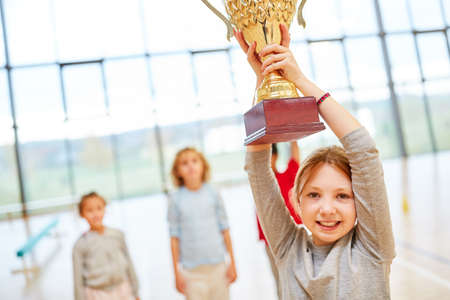 Happy girl proudly holds up the trophy at the award ceremony in schoolの写真素材