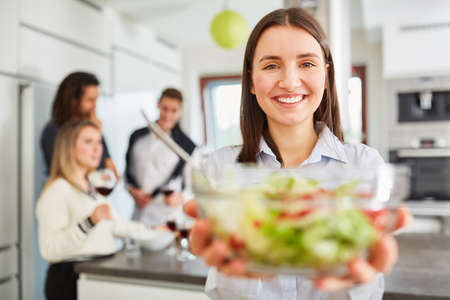 Young smiling woman in kitchen with a fresh bowl of lettuce in both hands