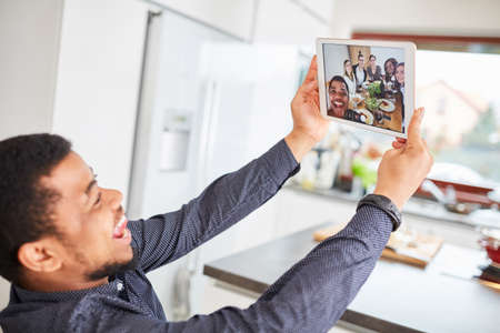 African man making selfie by group using tablet computer at meal at dining table