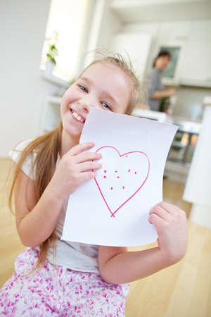 Happy girl shows a sheet of paper with a red heartの写真素材