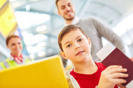 Boy with passport at check in counter in airport terminal with father in backgroundの写真素材