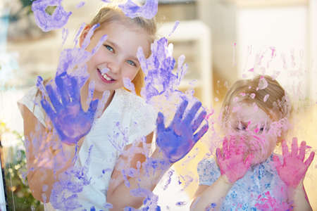 Two girls paint many handprints on a pane with finger paint
