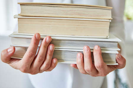 Woman carries stack of old books in her arms with hands