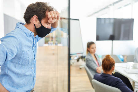 Thoughtful young businessman with face mask in office is stressedの写真素材