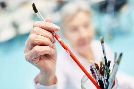 Senior takes a brush for painting in painting therapy at the retirement home