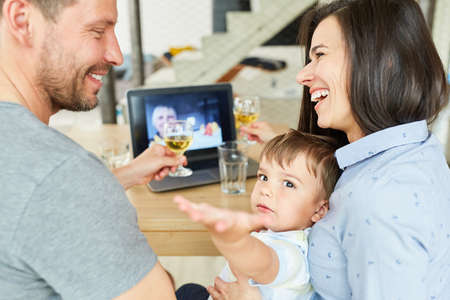 Happy couple with child drinking wine in video chat online on laptop computer