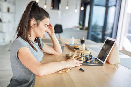 Woman playing chess at home thinks concentrated in video chat onlineの写真素材