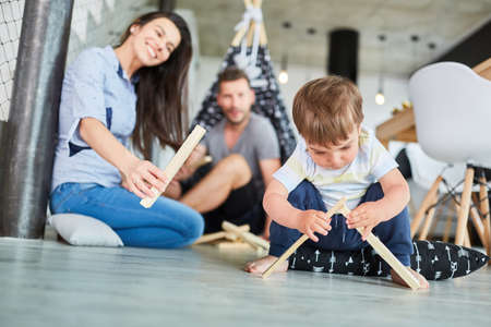 Parents help child pile wood for a campfire play during survival training