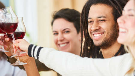 Happy friends sitting together at home sharing a glass of red wine in a shared apartment