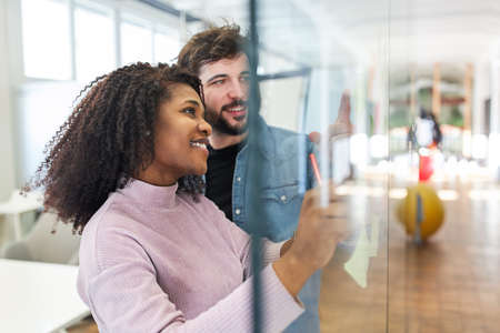 Creative team woman and colleague brainstorming on a glass wall of the internet agencyの写真素材