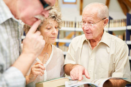 Three seniors read together in a book in the library in the retirement home