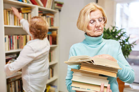 Elderly researches or reads a book in the library in the nursing homeの写真素材