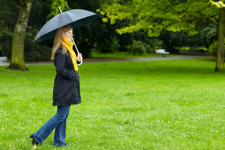 Blonde woman with umbrella in the rain on a green meadowの写真素材
