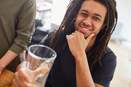African man with dreadlocks sits smiling at the dining table with friends over a meal