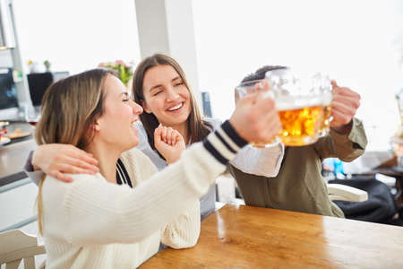 Happy group of women hug each other while watching football and clink glasses with beerの写真素材