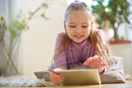 Child lies in the living room chatting on the Internet with a tablet PCの写真素材