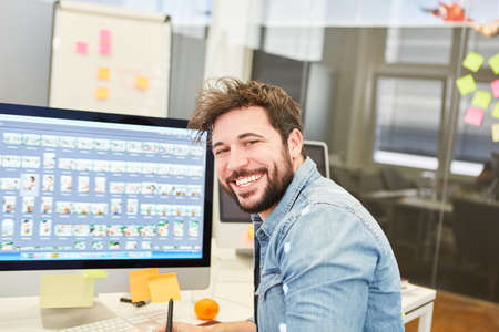 Graphic designer smiling on PC while designing a website in the design agency