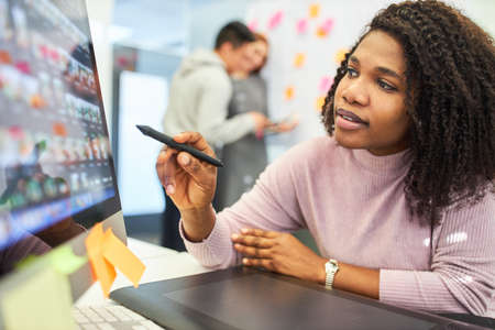 Creative African graphic designer with pen pointing at the computer monitor