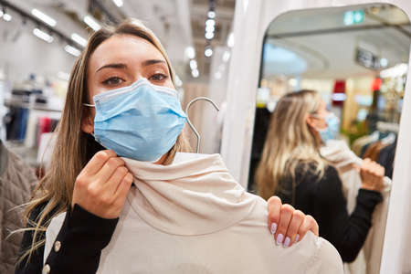 Woman as a customer with face mask in the Covid-19 pandemic in the locker room of a boutiqueの写真素材