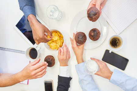 Hands of business people eating junk food like muffins and potato chips in the office