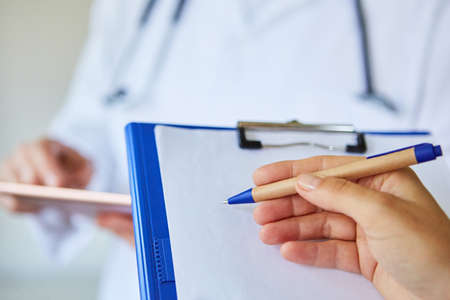 Doctor's hand with pen and clipboard makes notes for the medical recordの写真素材