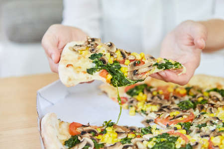 Hand with slice of pizza while eating a vegetable pizza as a vegan lunchの写真素材