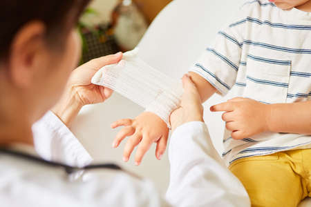 Pediatrician wraps bandage around child's wrist in the event of a sprain or accidentの写真素材
